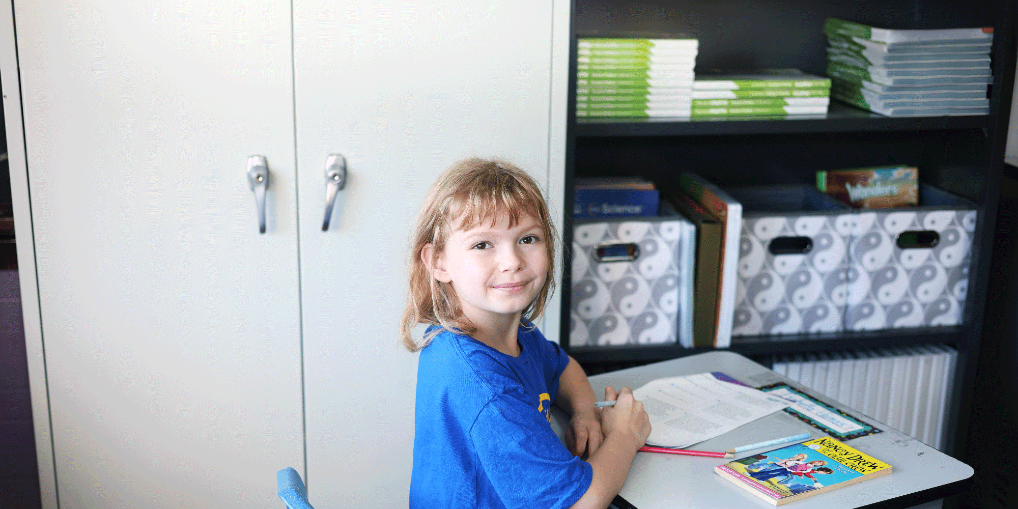 Student smiling at a desk with a workbook and pen.