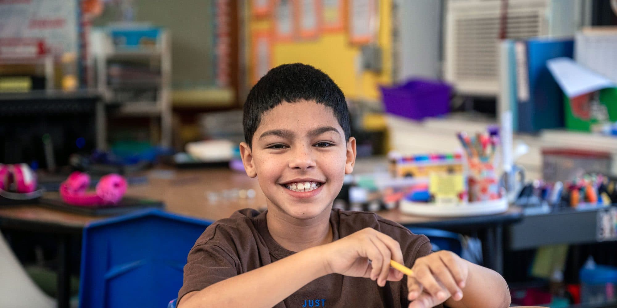 Smiling student holding a pencil at a classroom desk.