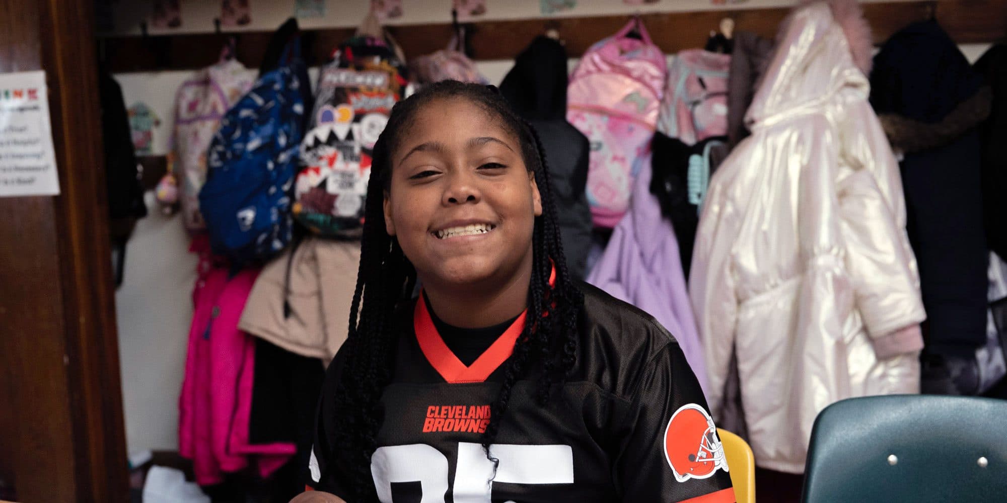 Smiling student in front of classroom coat hooks.