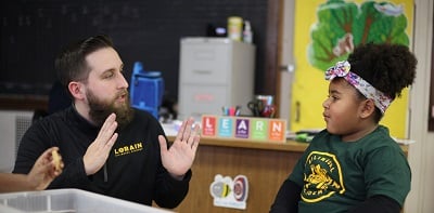 Adult and child talking at a table in a classroom.