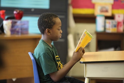 Child reading a book at a desk in a classroom.