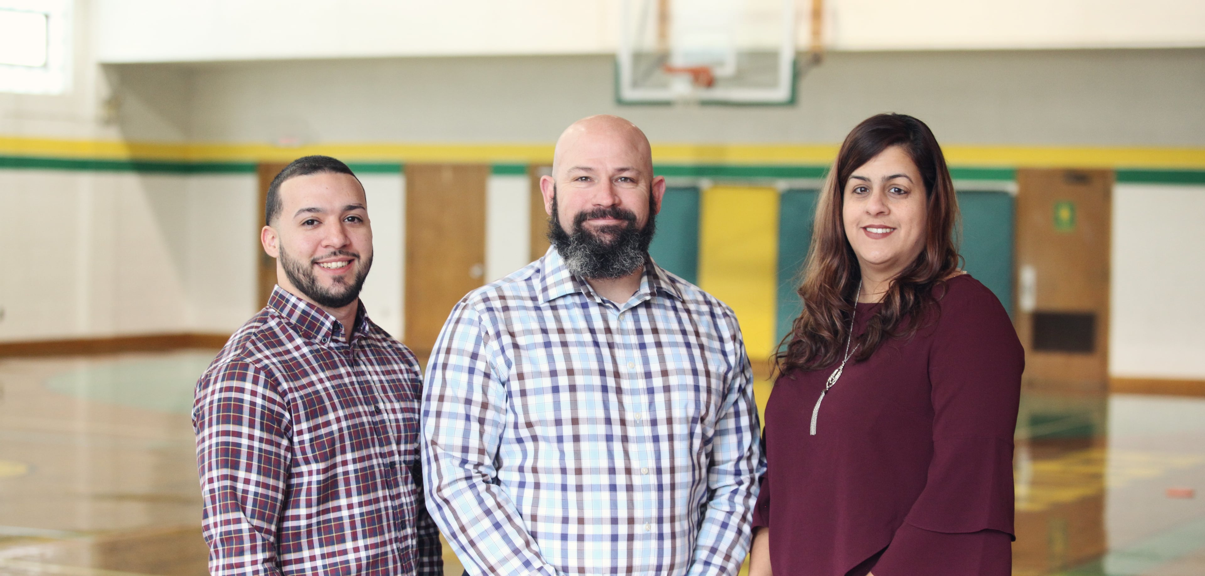Three smiling adults in a gymnasium.
